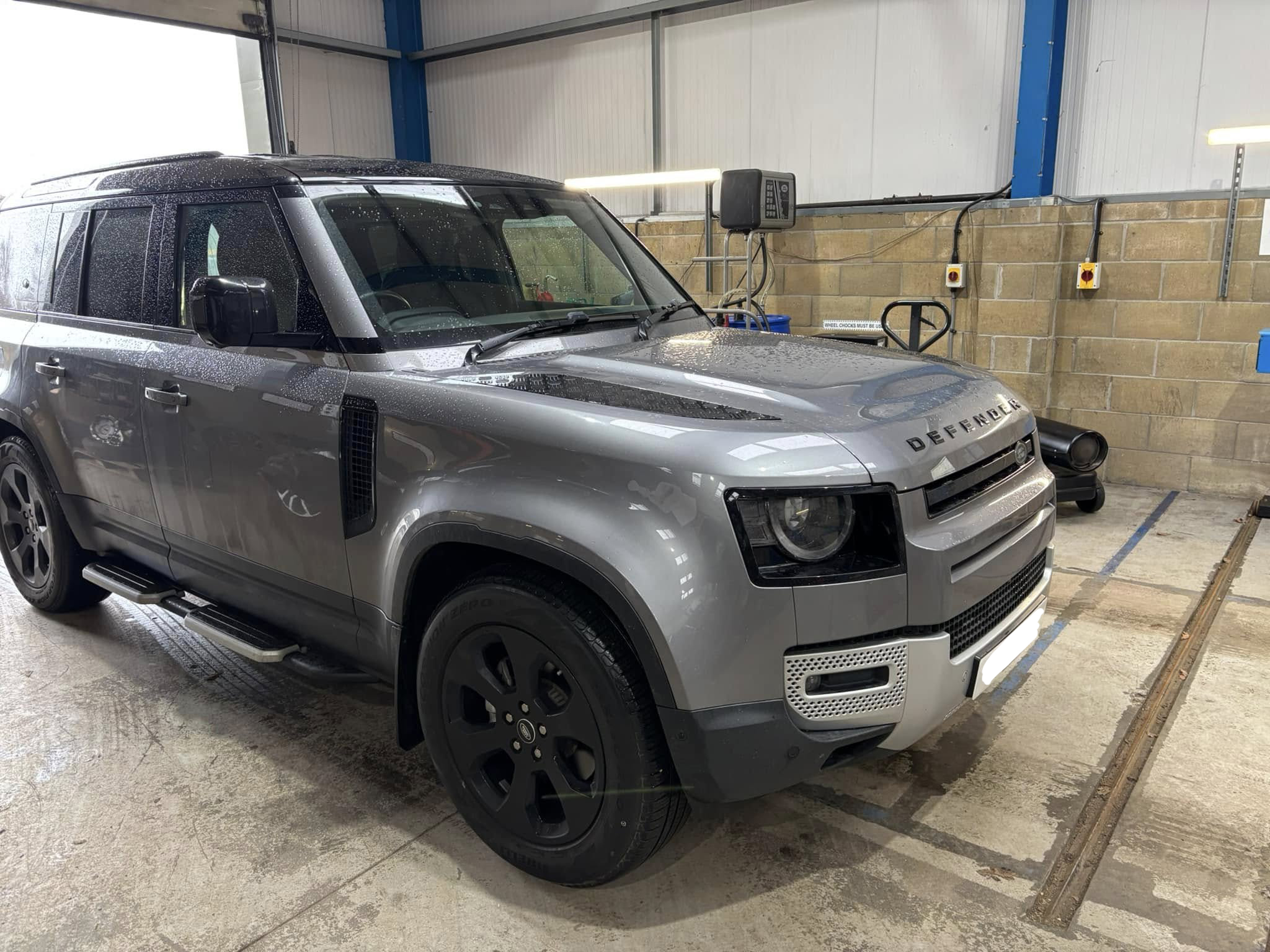 A freshly cleaned silver land rover defender in a mechanics garage