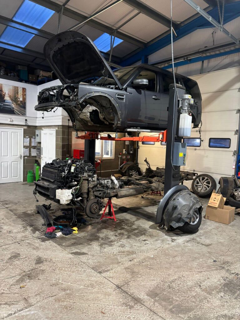 A dark grey land rover discovery, body has been separated from the frame and lifted by a four point lift.