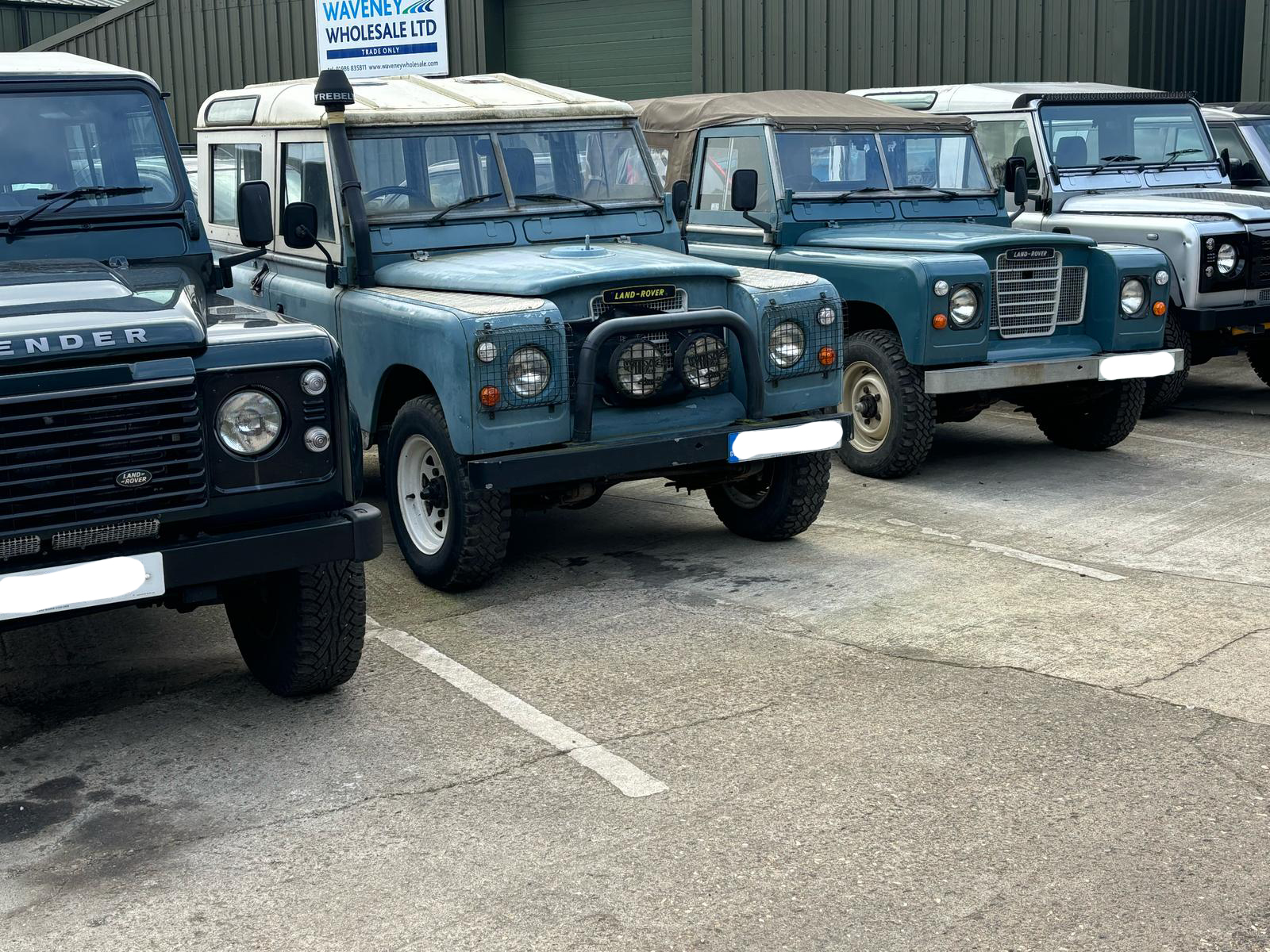 A series of older land rovers parked outside a garage