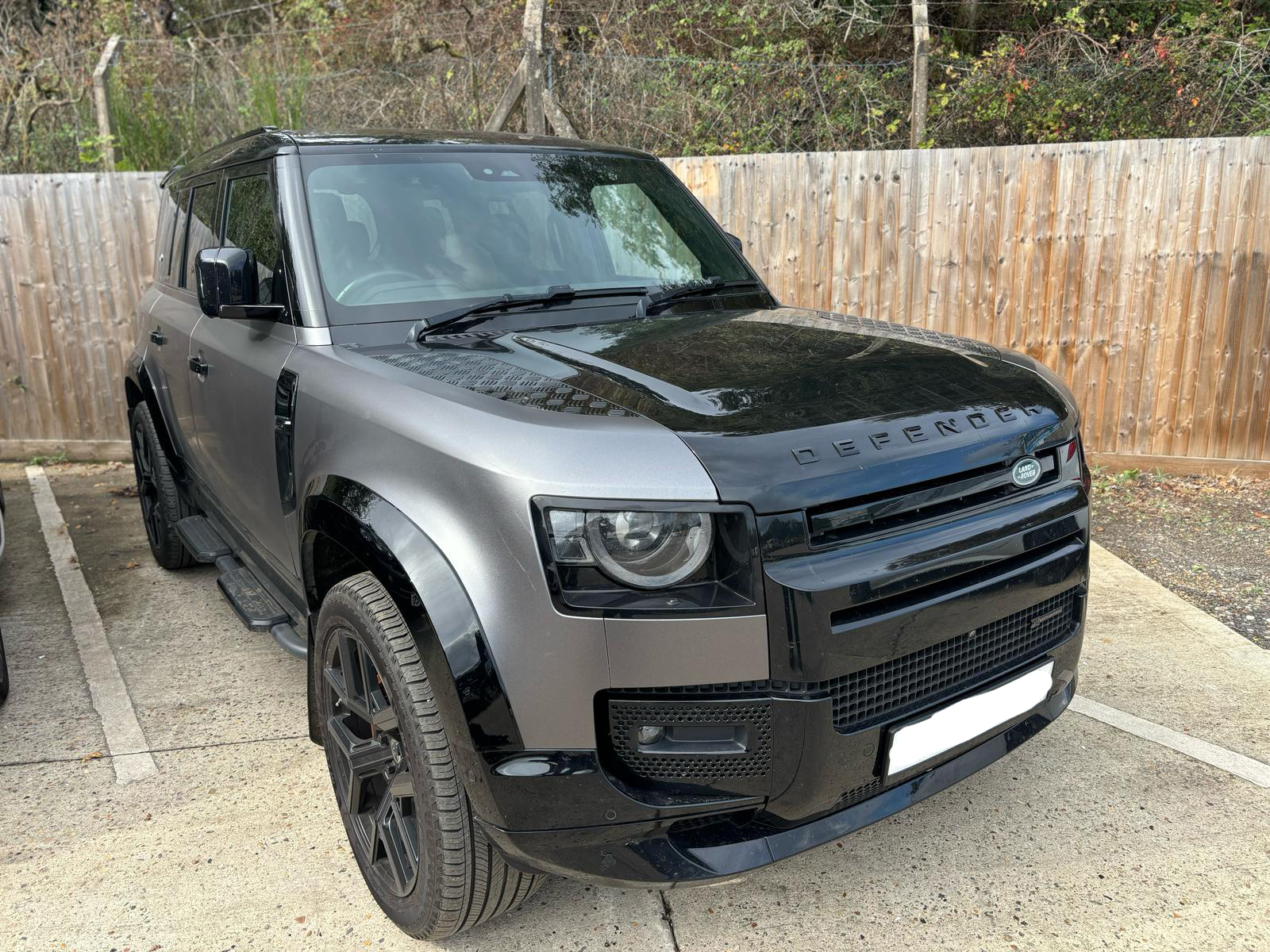 A new land rover defender parked outside in front of a fence